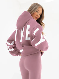 woman wearing a pink hoodie with BLAKELY printed on the back against a white background
