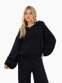 Woman wearing black ribbed knit hoodie and matching wide-leg pants on white background