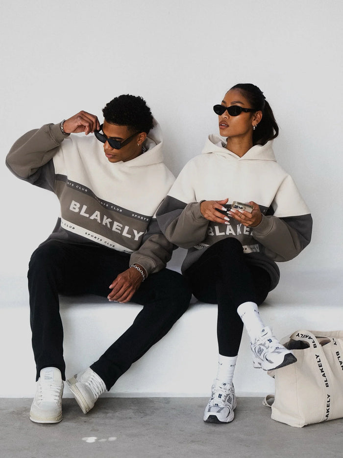 Two people wearing Blakely hoodies sitting on a white wall.